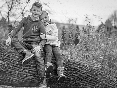 Geschwisterpaar auf Baumstamm sitzend